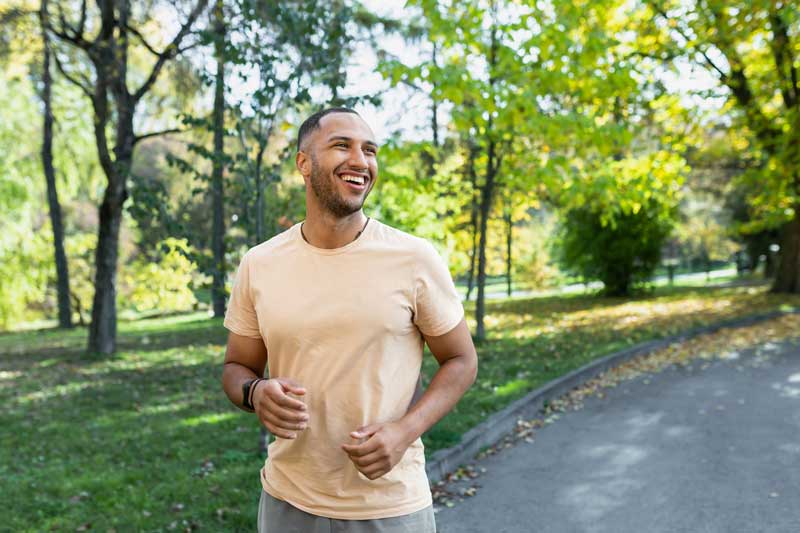Cheerful and successful hispanic man jogging in the park, man running on a sunny day, smiling and happy having an outdoor activity